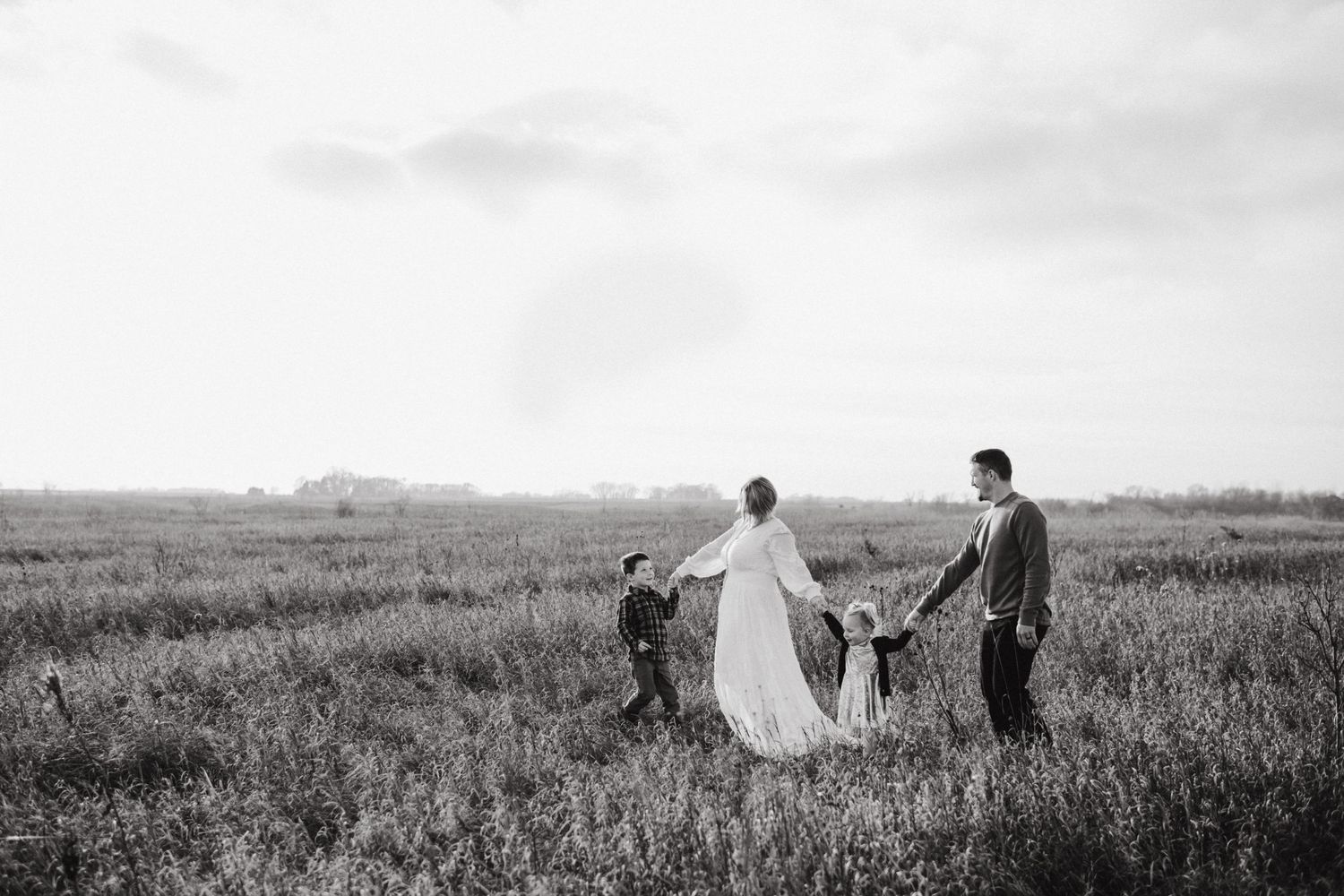 A family holds hands while walking together through a scenic prairie landscape.