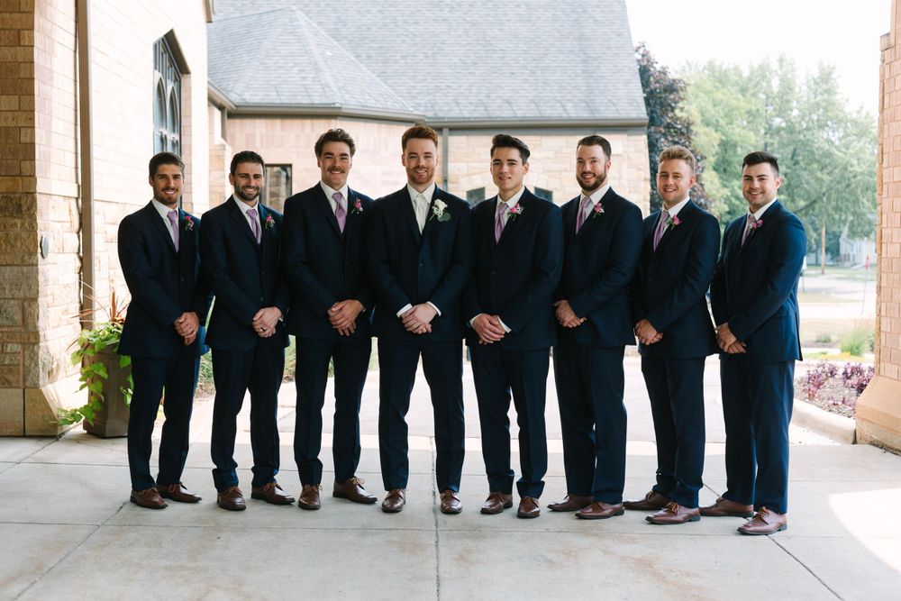 Groomsmen in black suits lined up formally outside church entrance.