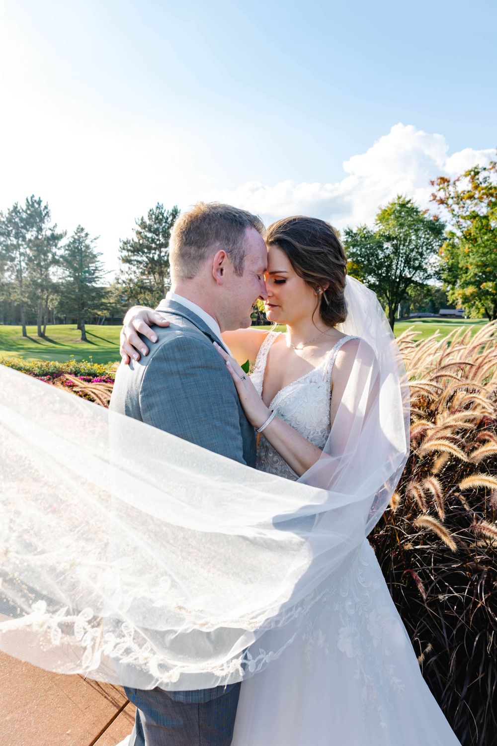 A romantic wedding portrait with flowing veil caught in the breeze against a sunset garden backdrop.