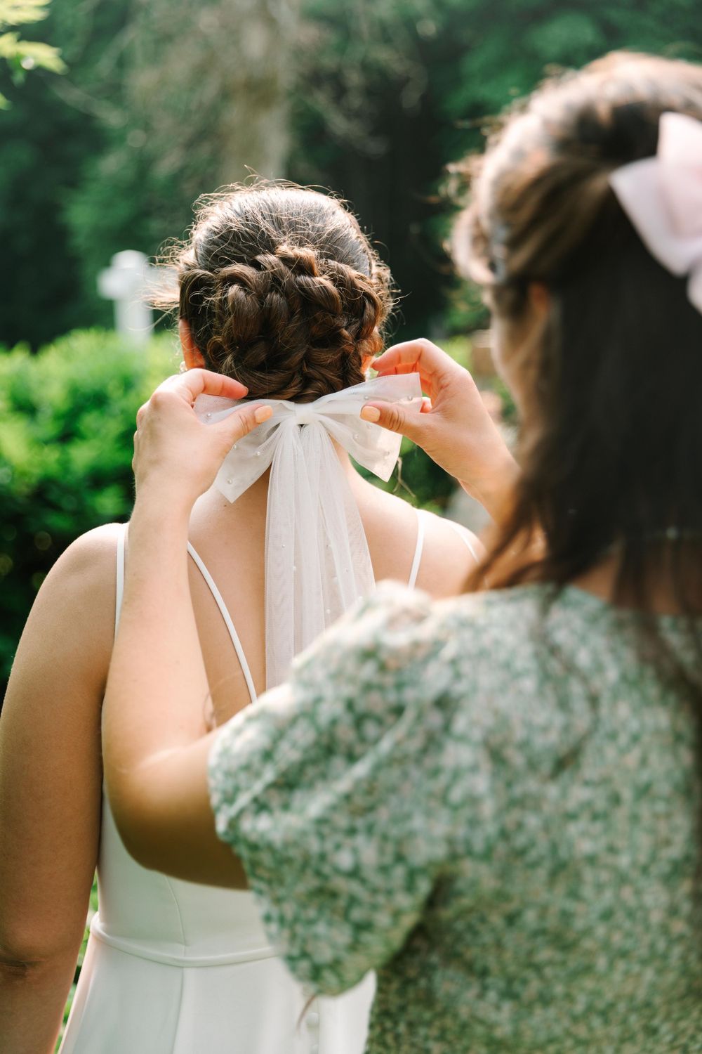 A bridesmaid helps adjust a white bow detail on a bride's wedding dress.