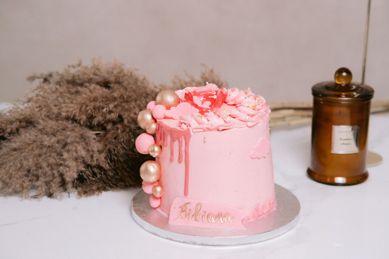 Pink drip cake with metallic decorations and elegant floral details.