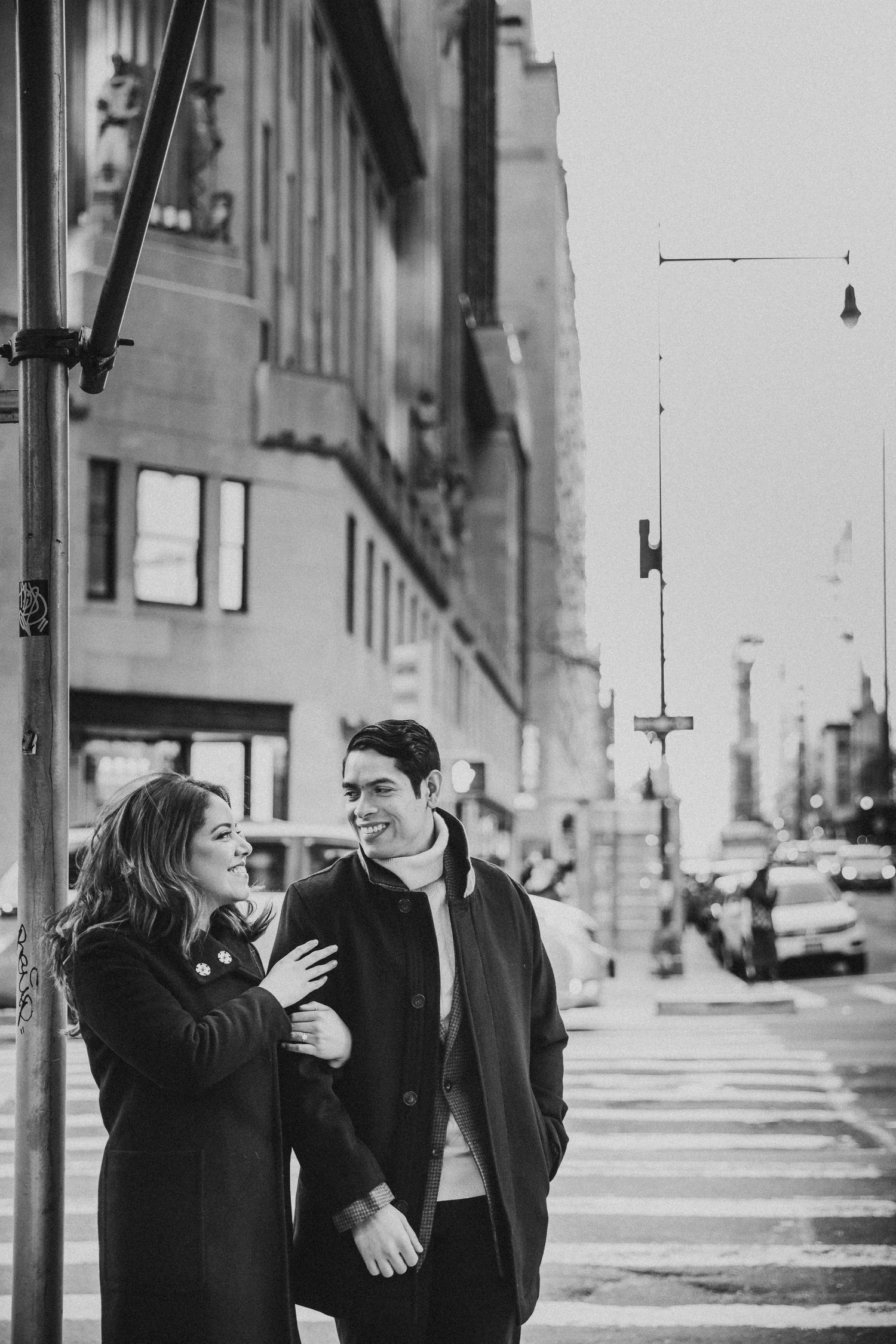 Black and white photo of a couple smiling and embracing on a city street corner.