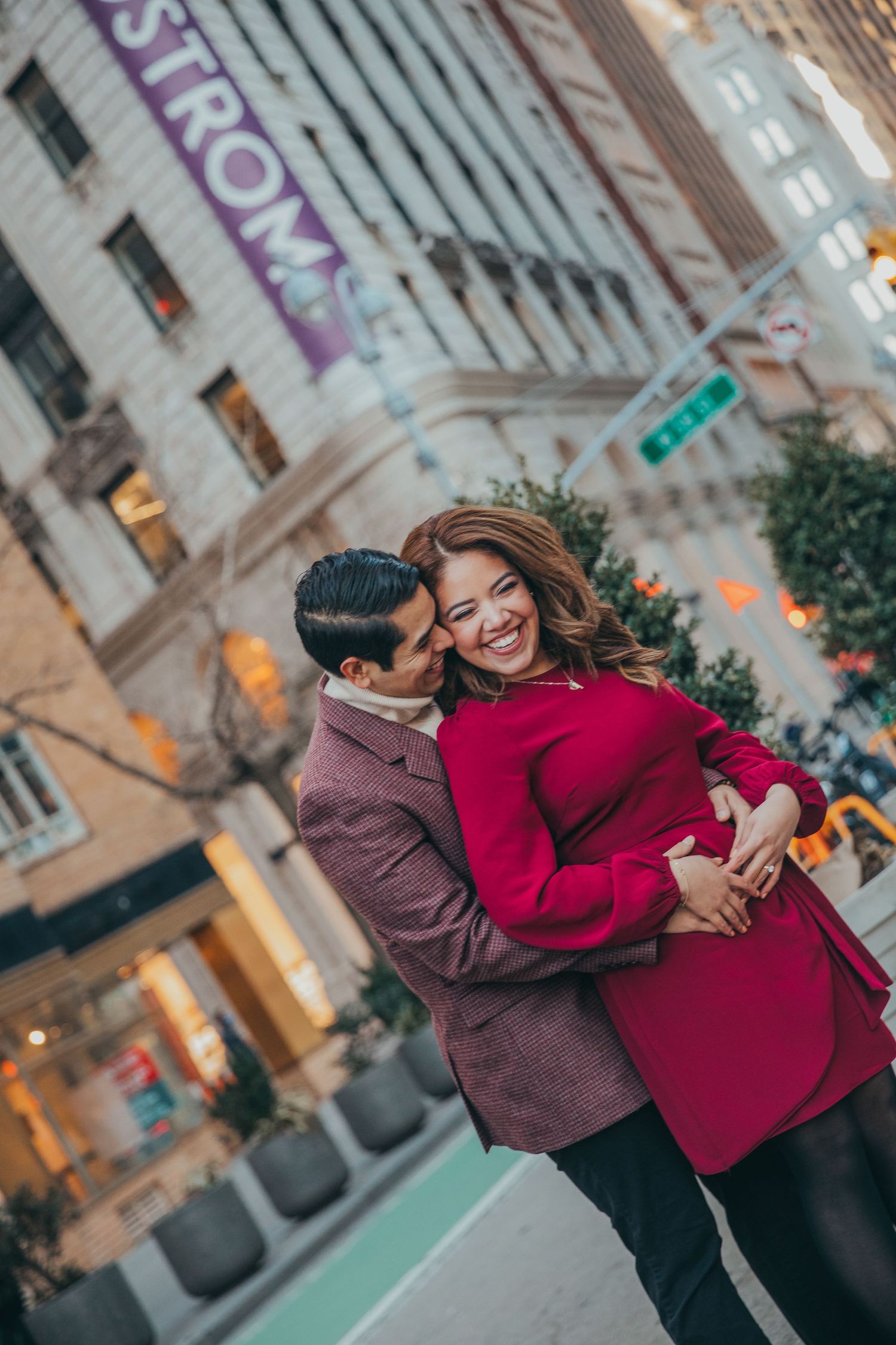 Man embracing woman in red coat from behind near Nordstrom store on a New York City street.