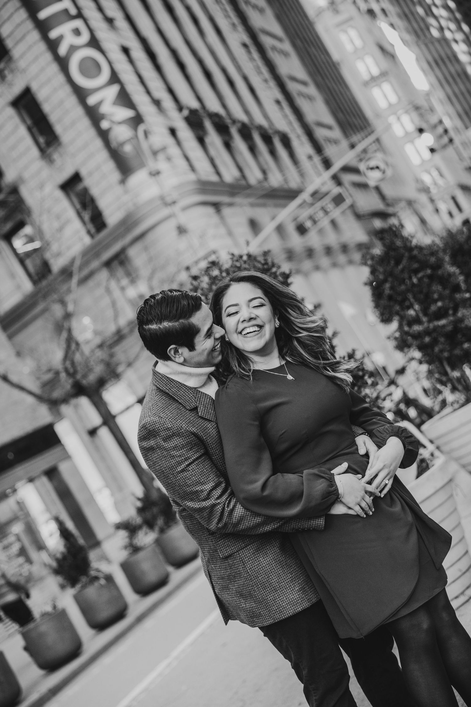 Black and white photo of a couple hugging and laughing outside a Nordstrom store.