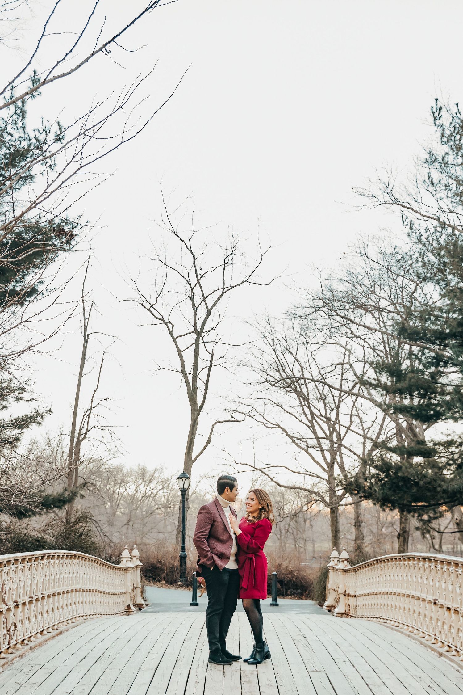 Couple facing each other romantically on a white ornamental bridge in Central Park in winter.