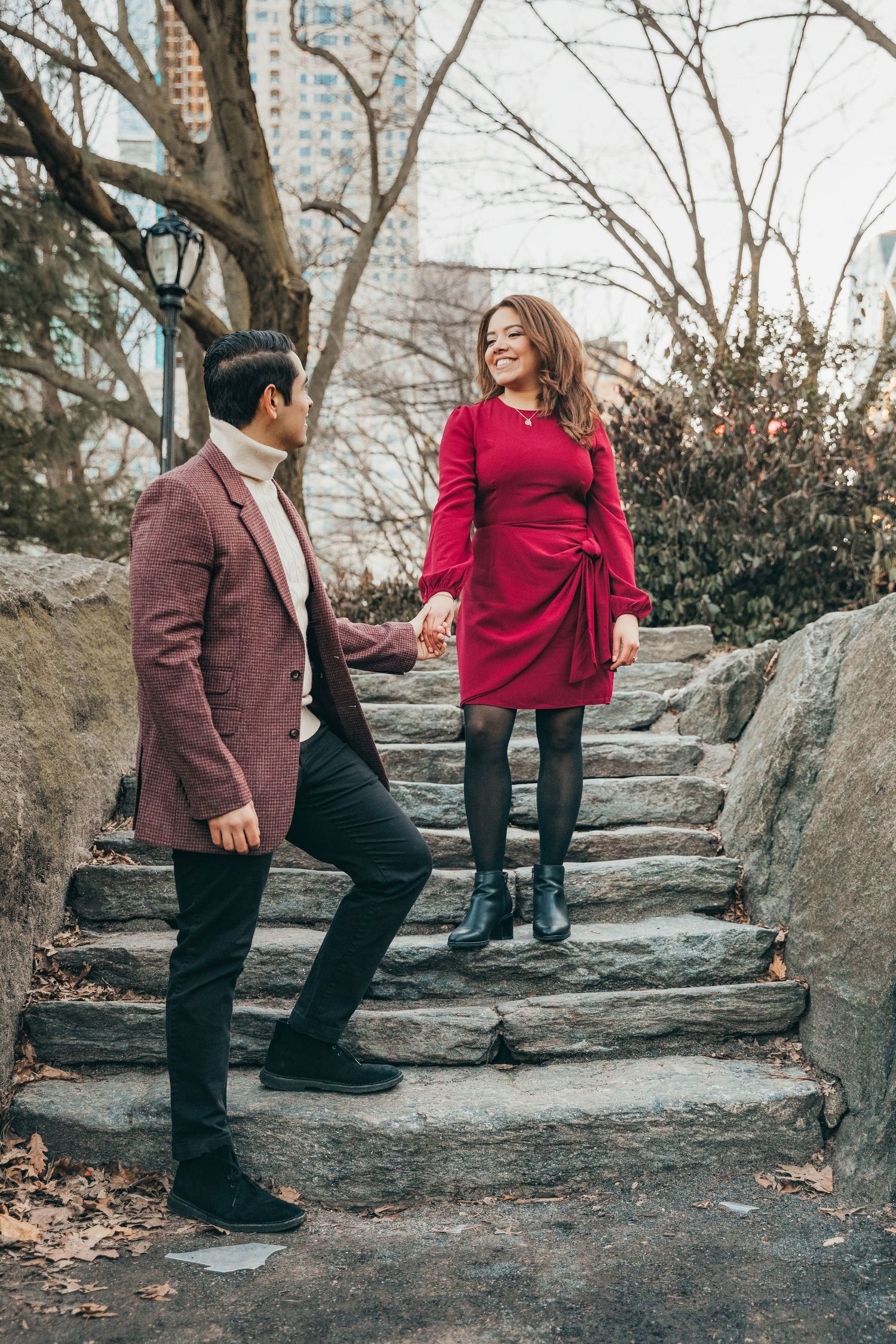 Couple holding hands on stone stairs in Central Park, woman in red dress smiling at partner.