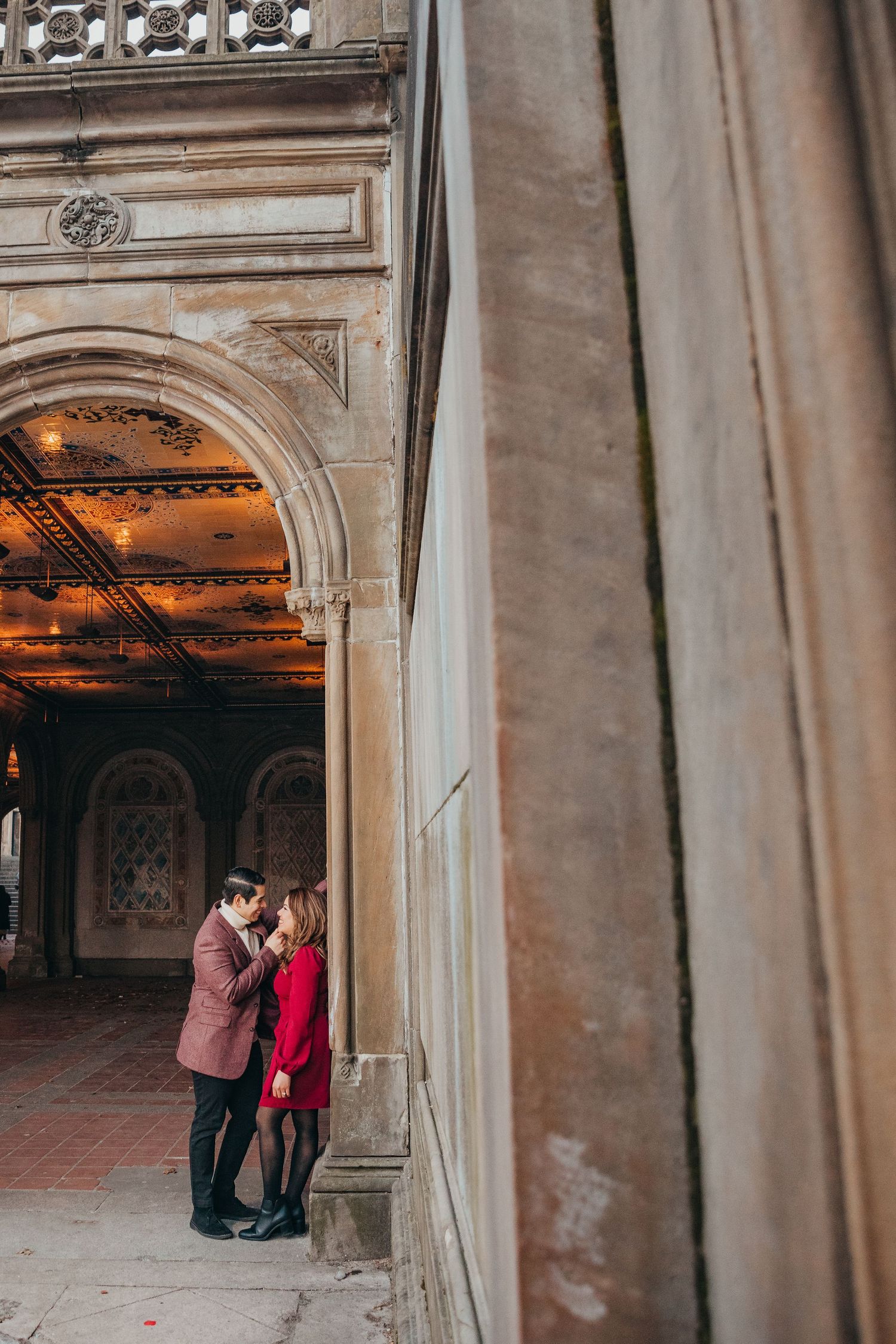 Couple sharing an intimate moment framed by the historic stone arches of Bethesda Terrace in Central Park.