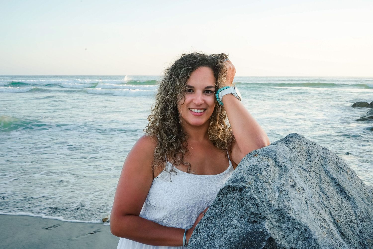 Beach photoshoot with waves crashing against rocks during sunset.