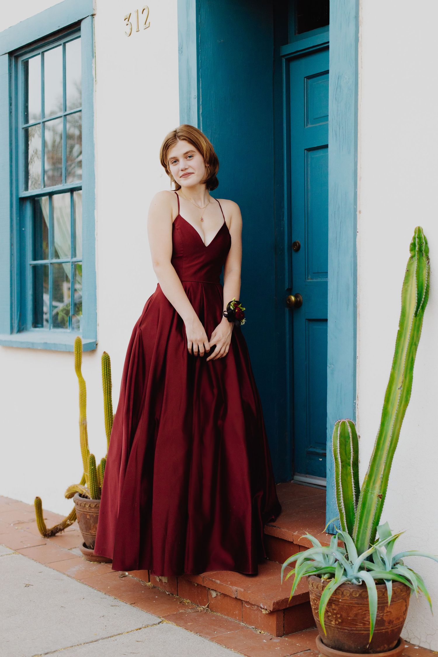 A burgundy dress photographed against white adobe walls with blue trim and potted cacti.