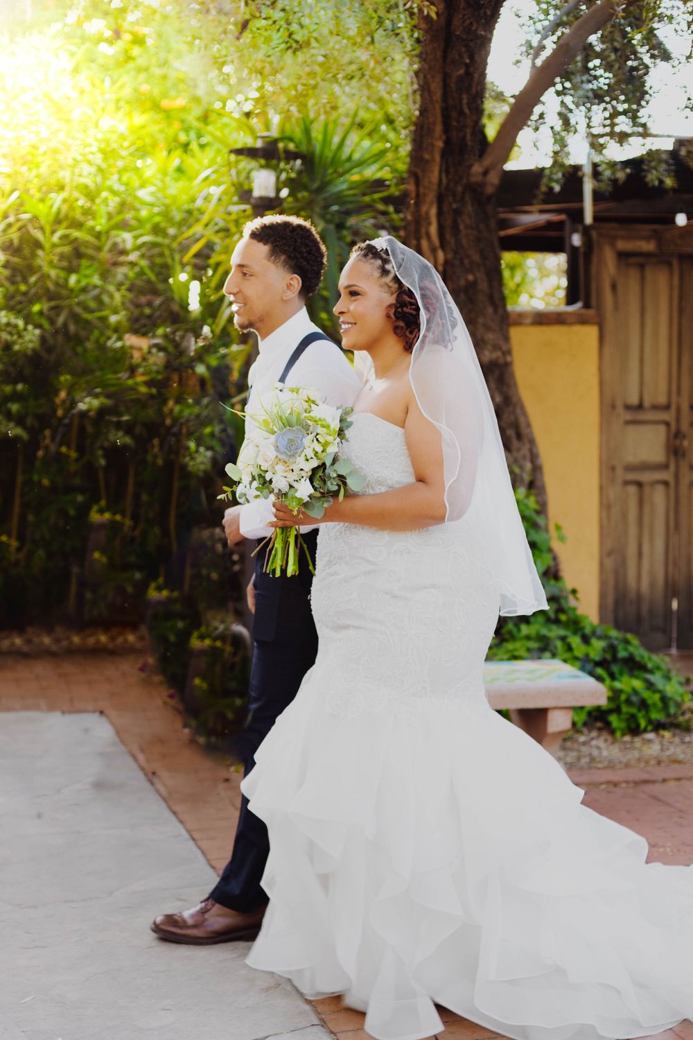 Couple walks together during their garden wedding with white floral bouquet.