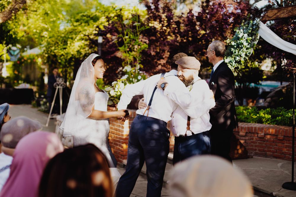 A joyful outdoor wedding ceremony taking place in a garden setting with string lights and trees.