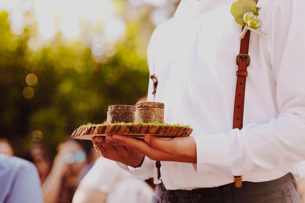 Server holds wooden tray with drinks during outdoor wedding reception.