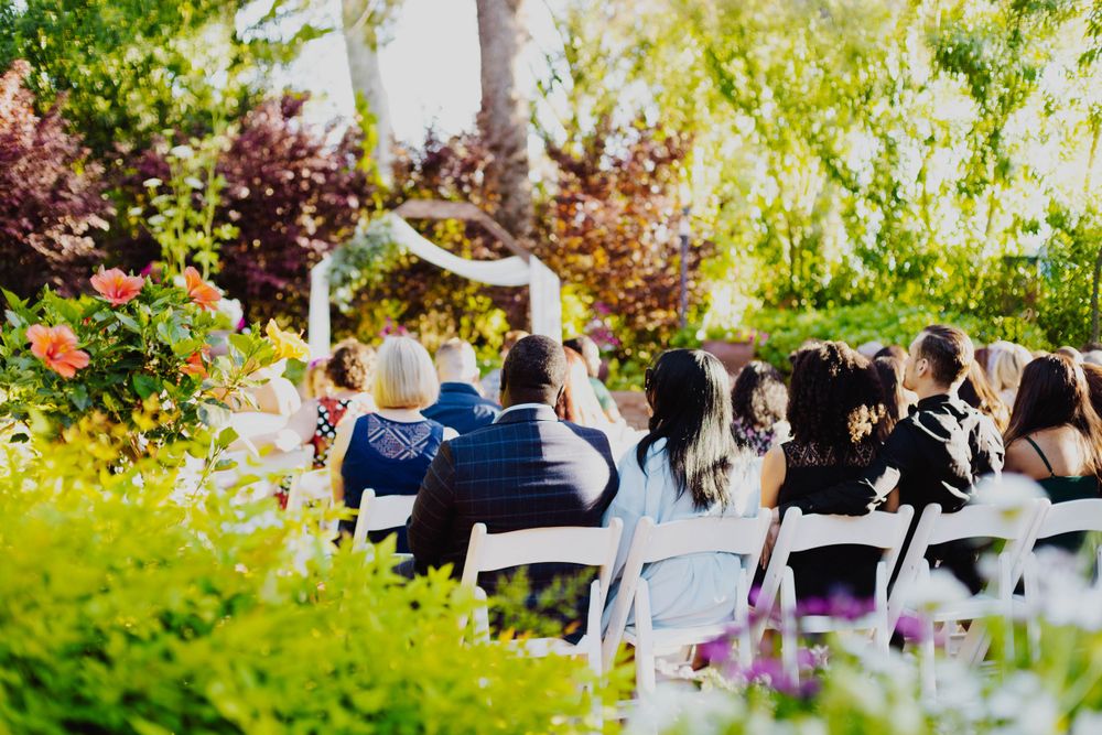 Outdoor wedding ceremony setup with white chairs surrounded by lush gardens and trees.