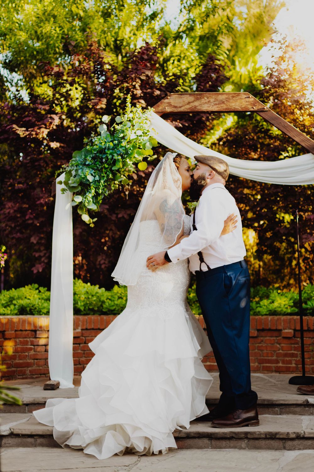 Romantic wedding moment under white draped arch with garden backdrop.