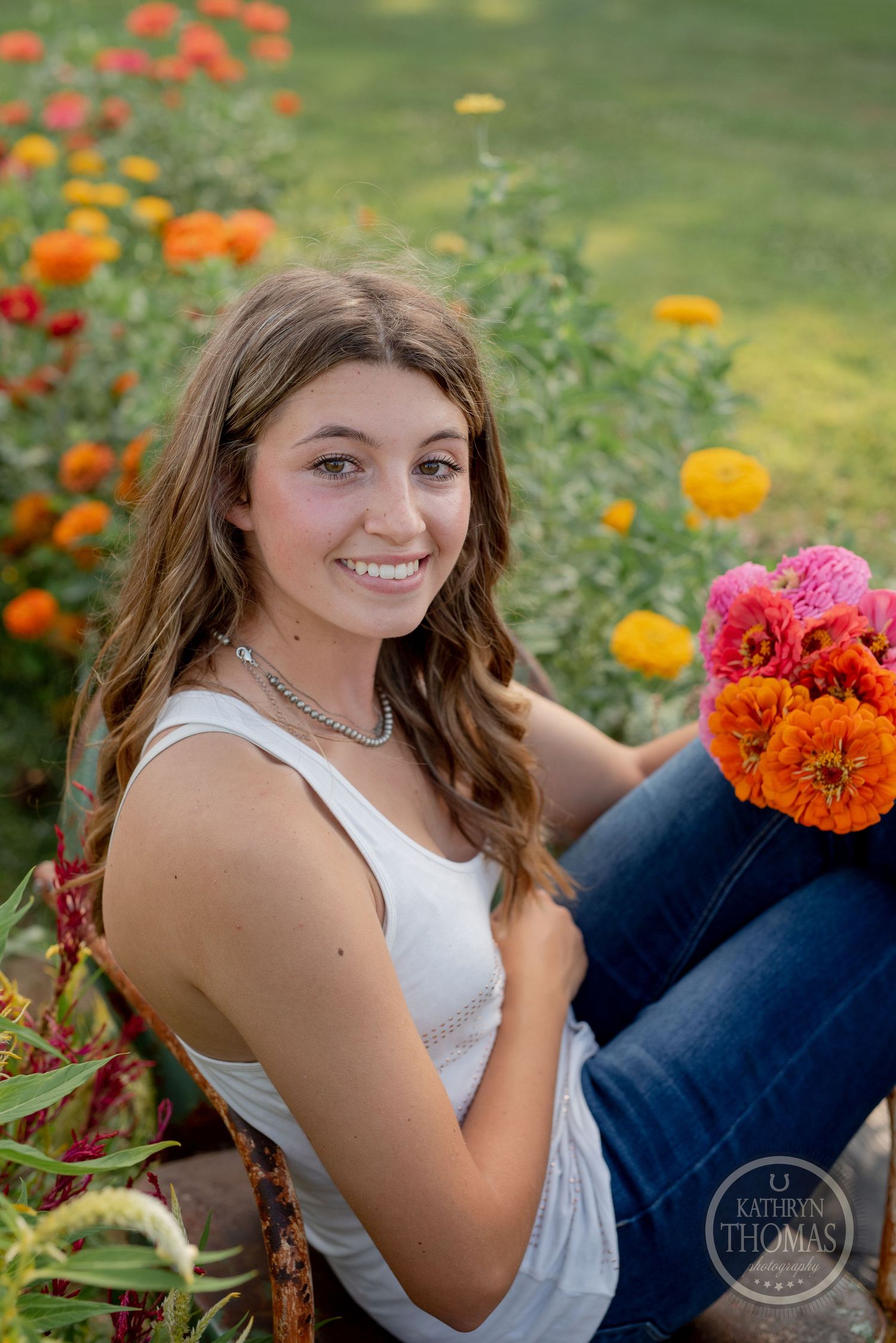 Person holding bright orange zinnia bouquet while sitting in summer flower garden.