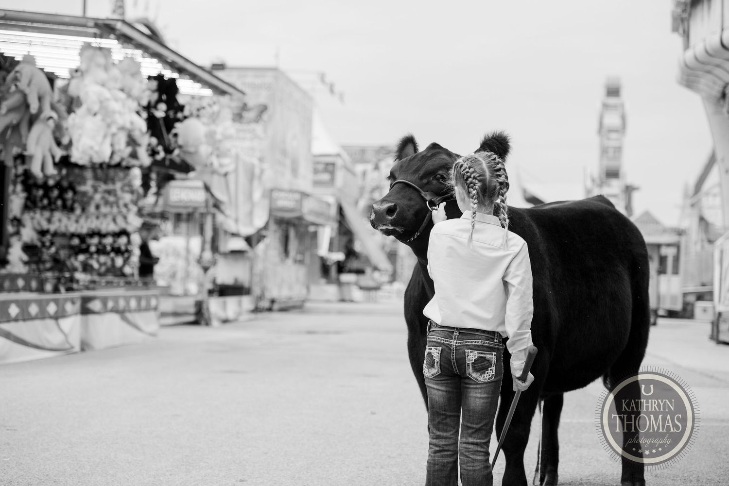 A black and white photo shows a figure with a horse at a carnival midway.