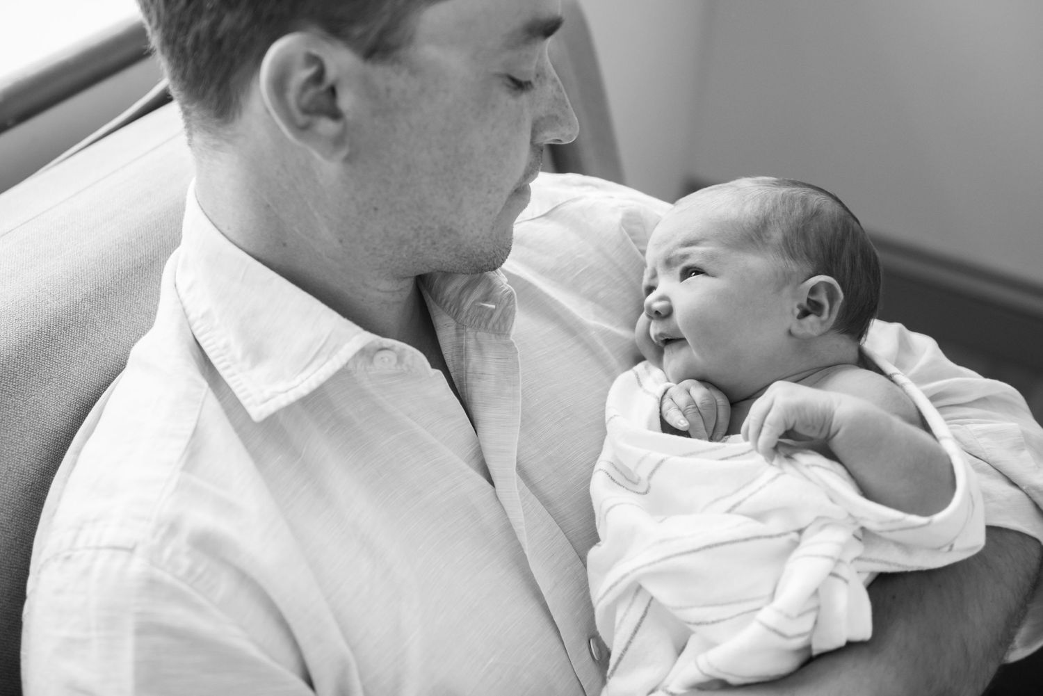 An intimate black and white photograph showing a tender moment between a parent and infant.