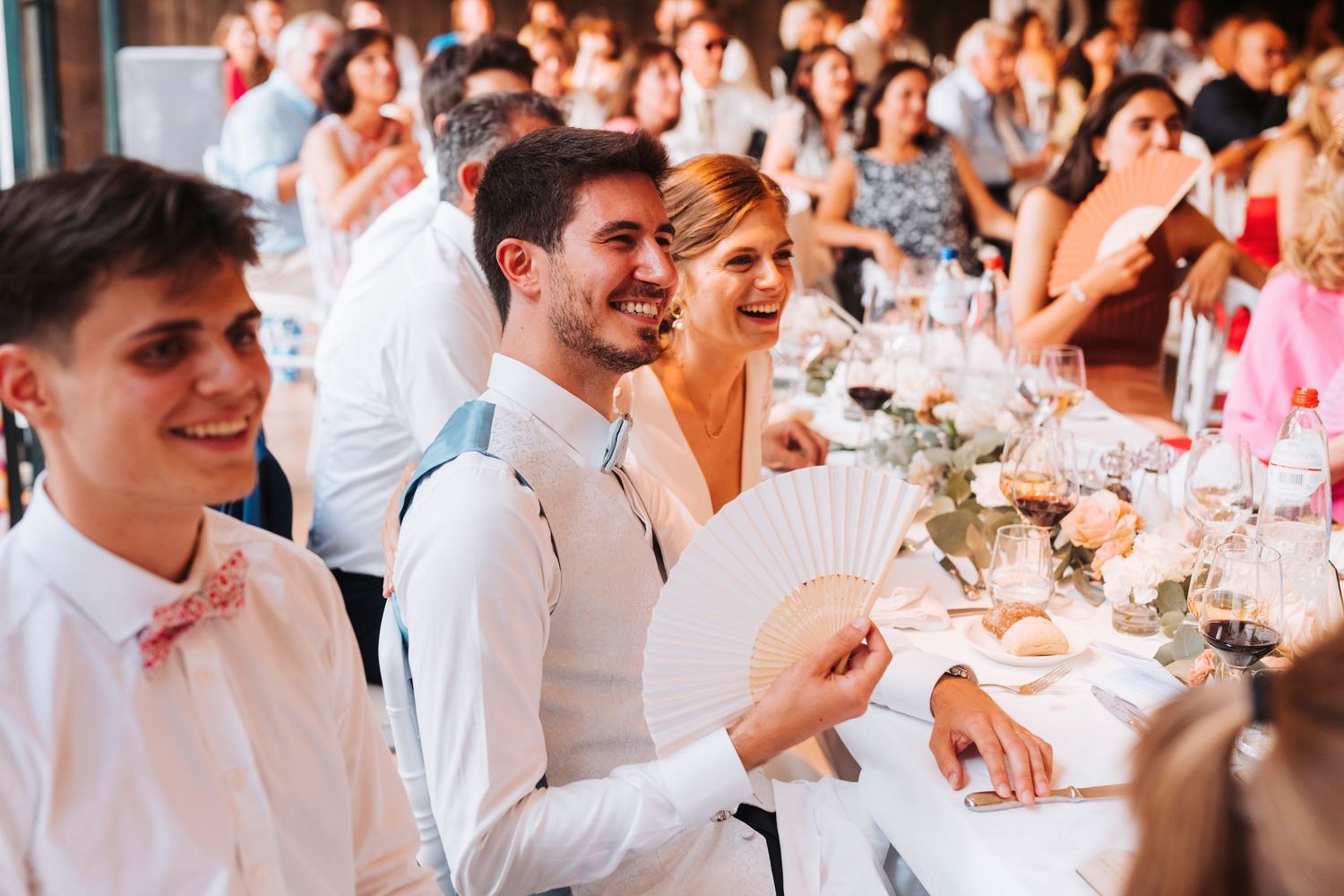 Wedding guests enjoying reception dinner with decorative hand fans.