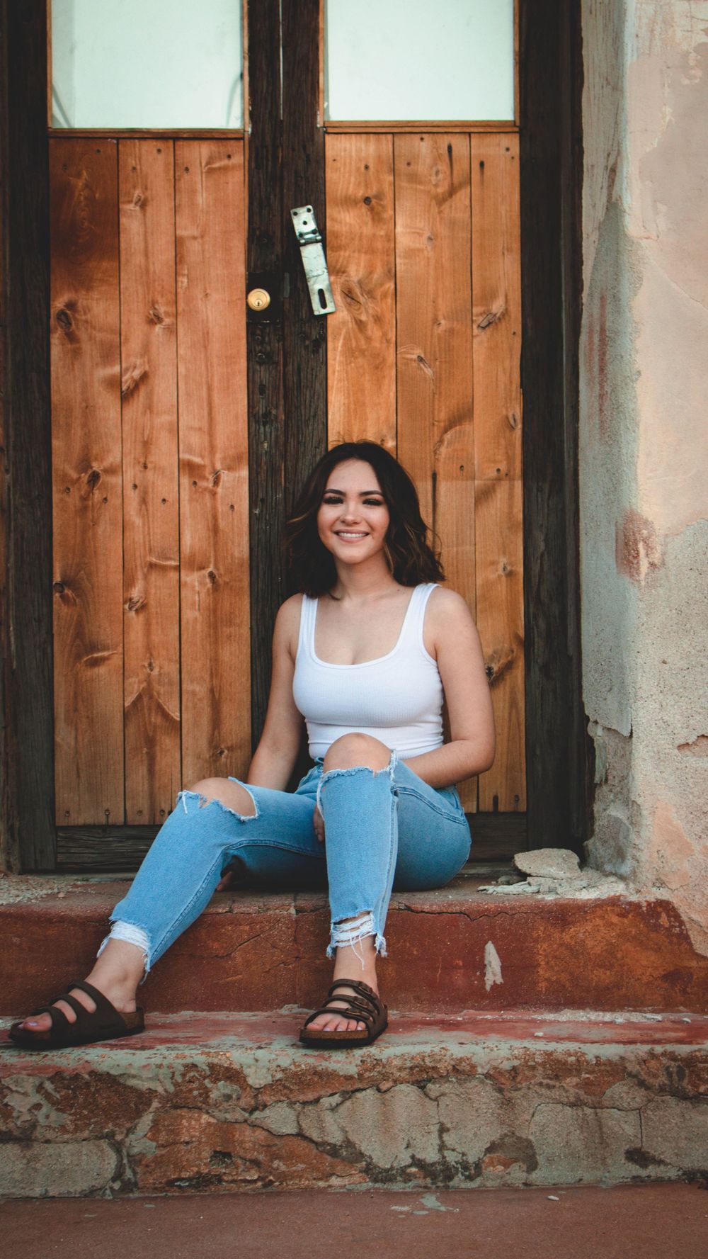 Casual portrait session against rustic wooden doors and stone wall.