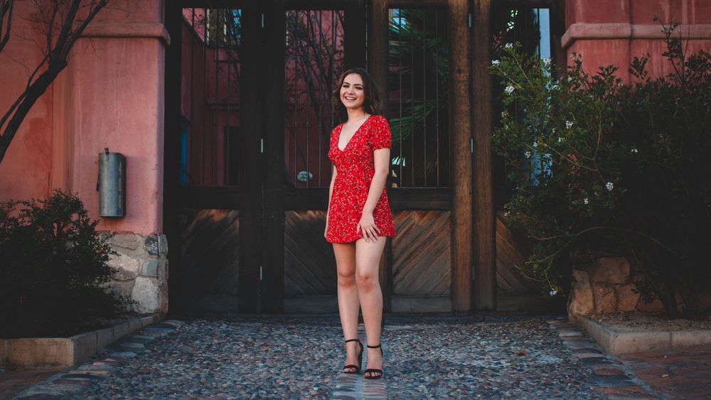 Person in red dress walking along cobblestone street with rustic buildings and greenery.
