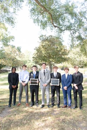 Formal group photo of young people holding chalkboard signs under trees.