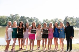 Group in colorful dresses and formal wear pose together by a lake.