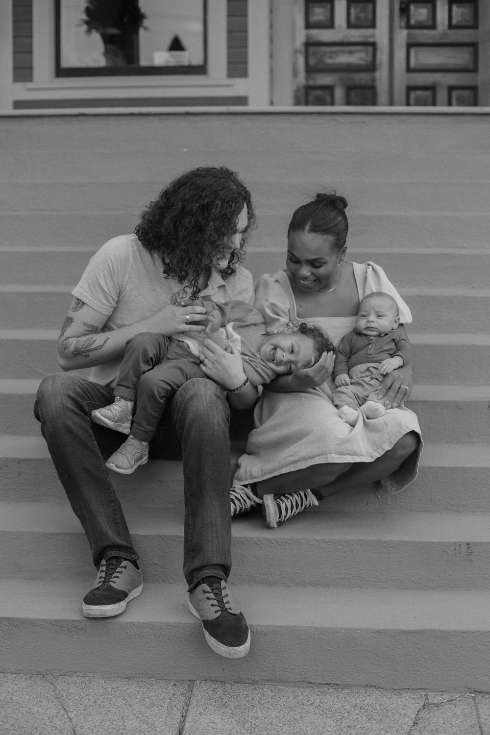 A couple sitting on outdoor steps sharing a tender moment with their baby in a black and white photograph.