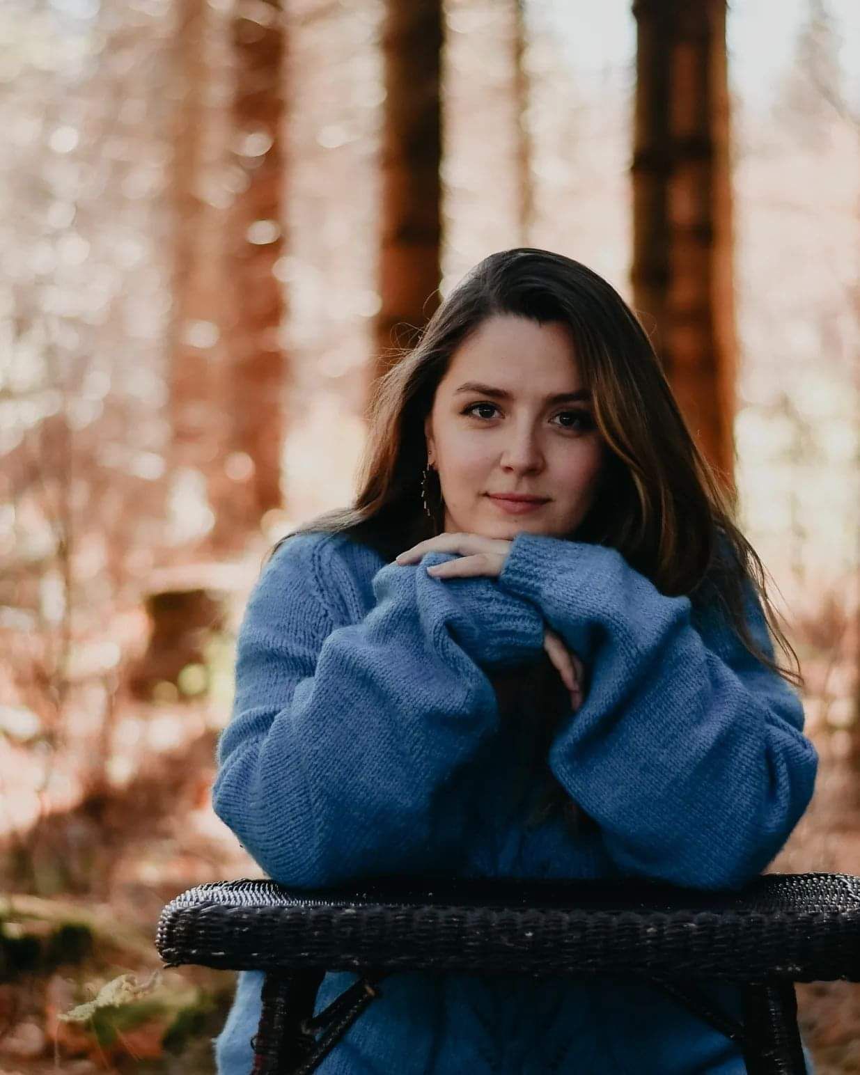 Person in blue sweater resting on bench in forest setting.
