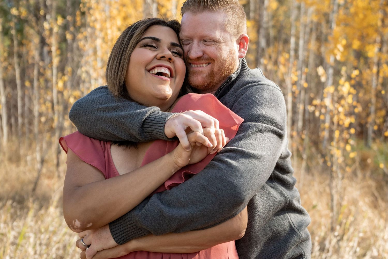 Couple sharing a loving embrace and laughter against a backdrop of autumn trees.