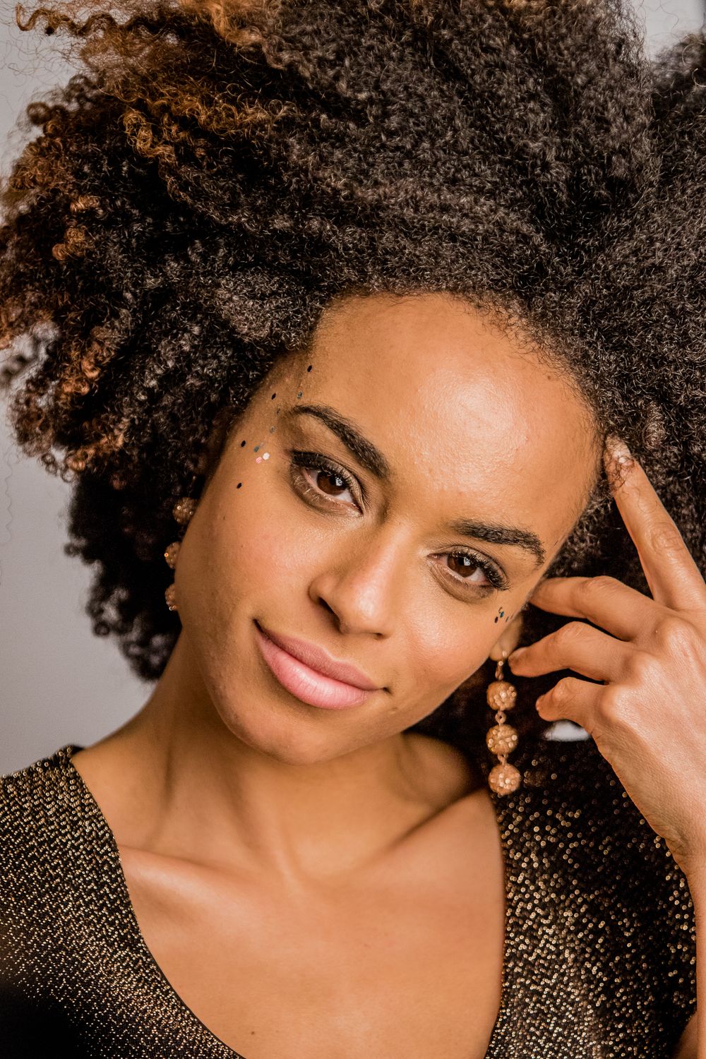 Close-up portrait of woman with natural curly afro hair wearing gold earrings touching temple.