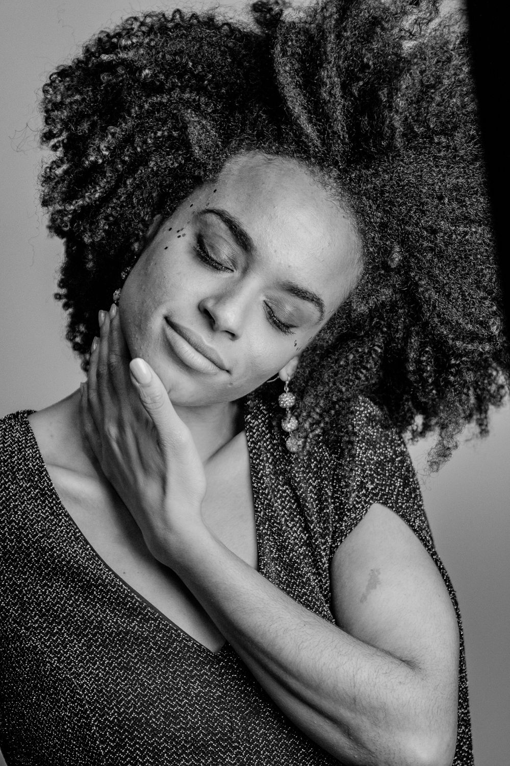 Black and white portrait of woman with natural curly hair resting face on hand eyes closed.