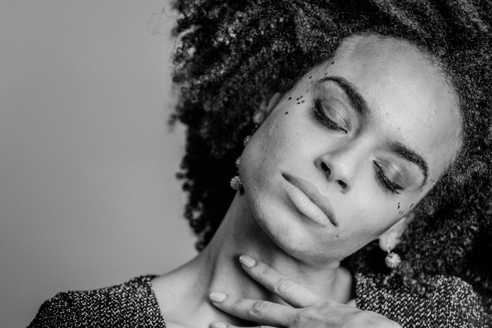 Black and white portrait of woman with natural curly hair and closed eyes touching her neck.