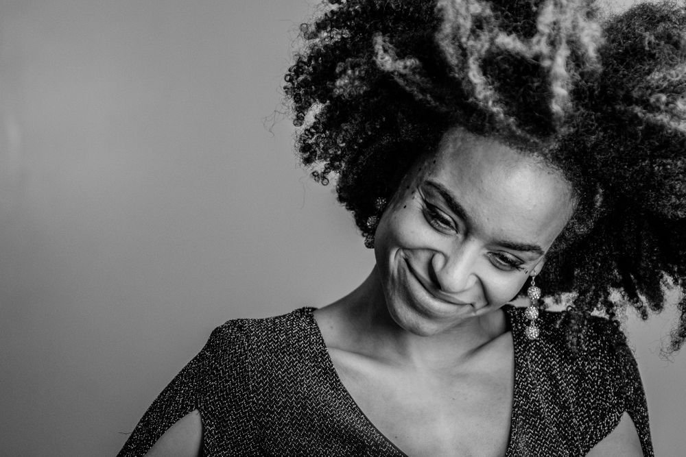 Black and white portrait of smiling woman with voluminous natural afro hair looking downward.