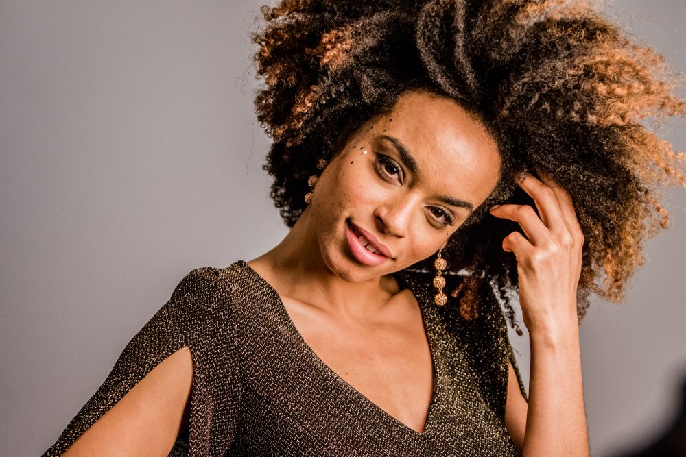 Young Black woman with natural curly afro hair wearing gold earrings and sparkly top portrait.