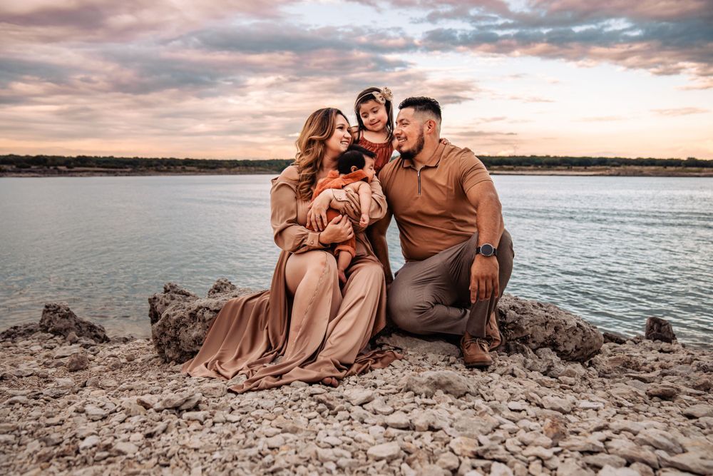 Mother and father sitting on rocks near water holding baby with young daughter looking at them