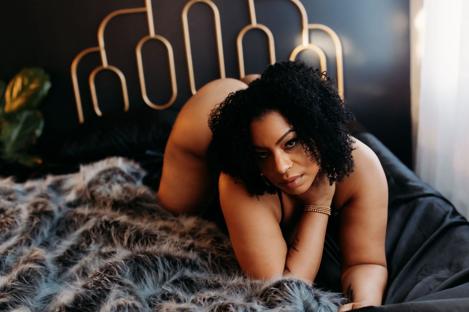 Artistic boudoir photography with dark bed linens and unique metallic headboard.