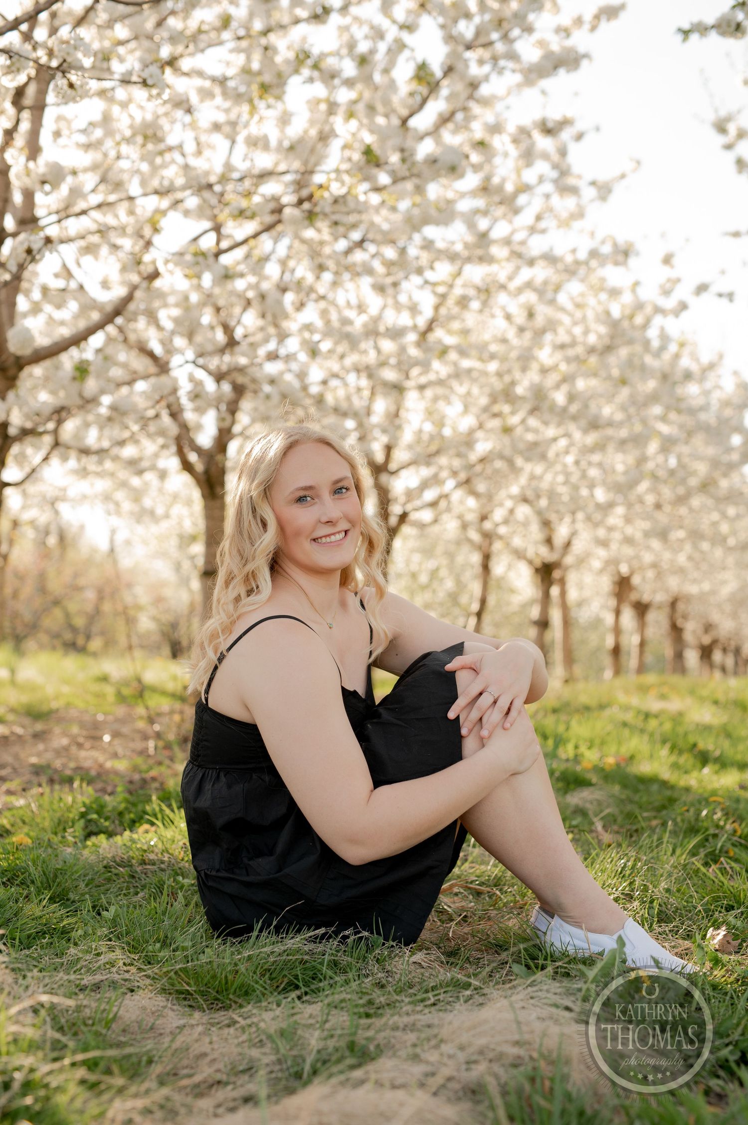 Casual outdoor portrait session among rows of blooming spring trees.