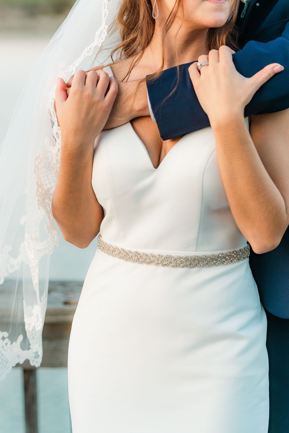 Close-up detail of an elegant white wedding dress with beaded belt and lace veil.
