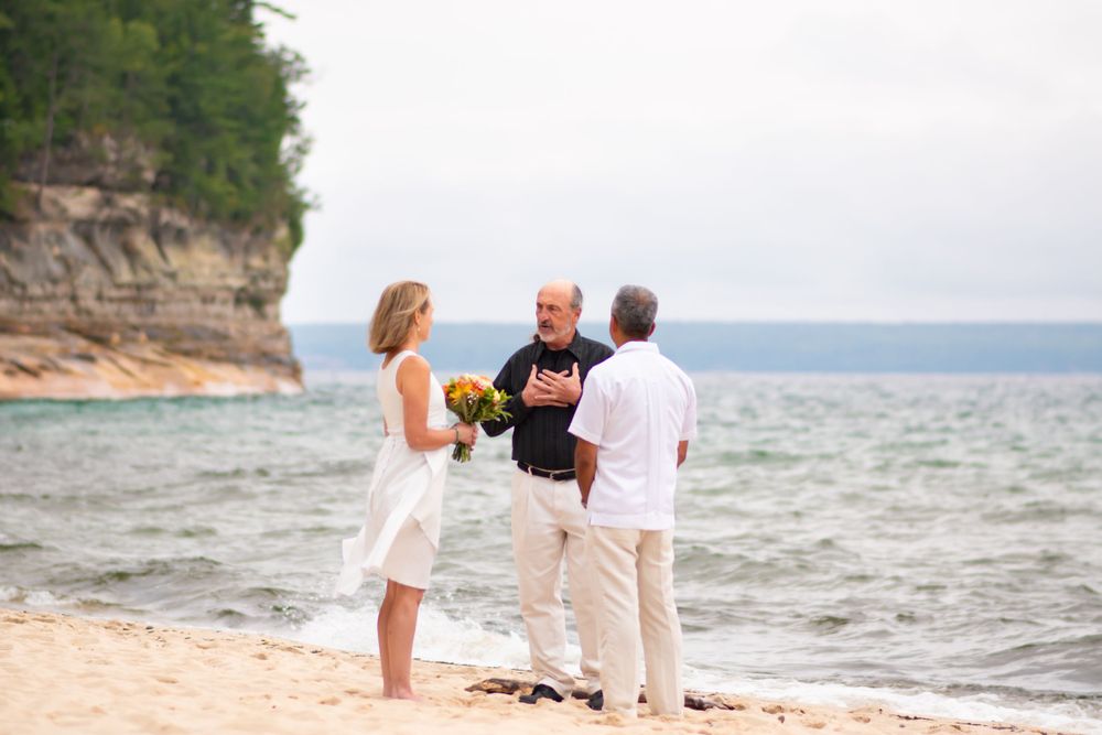 Beach wedding ceremony on sandy shore with cliffs and water in background.