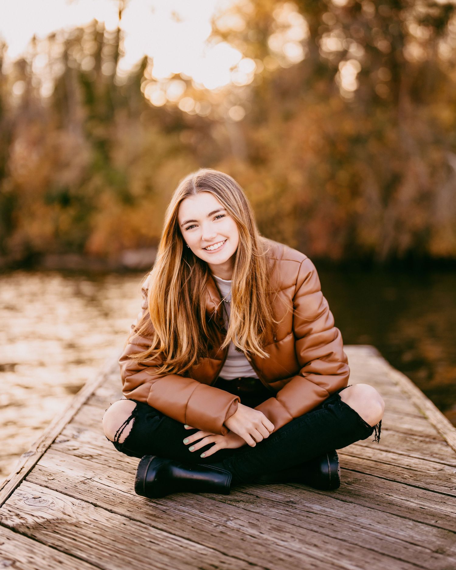 High school senior girl smiling on a dock at sunset