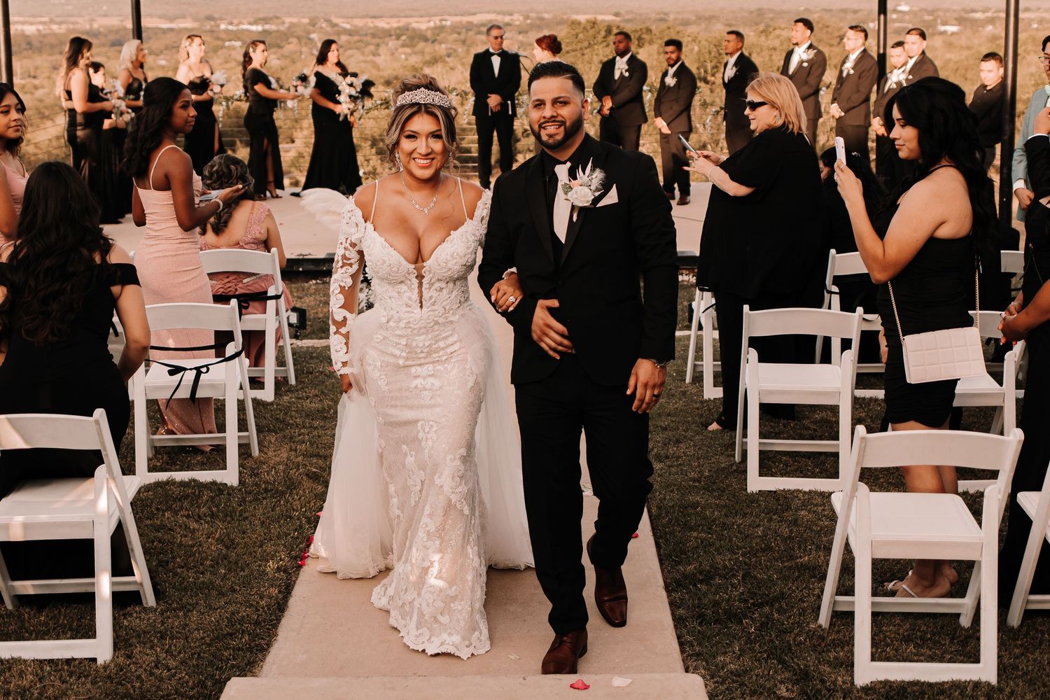 Bride in lace gown and groom in black tuxedo walking down the aisle at outdoor wedding ceremony taken by Houston Photographer.