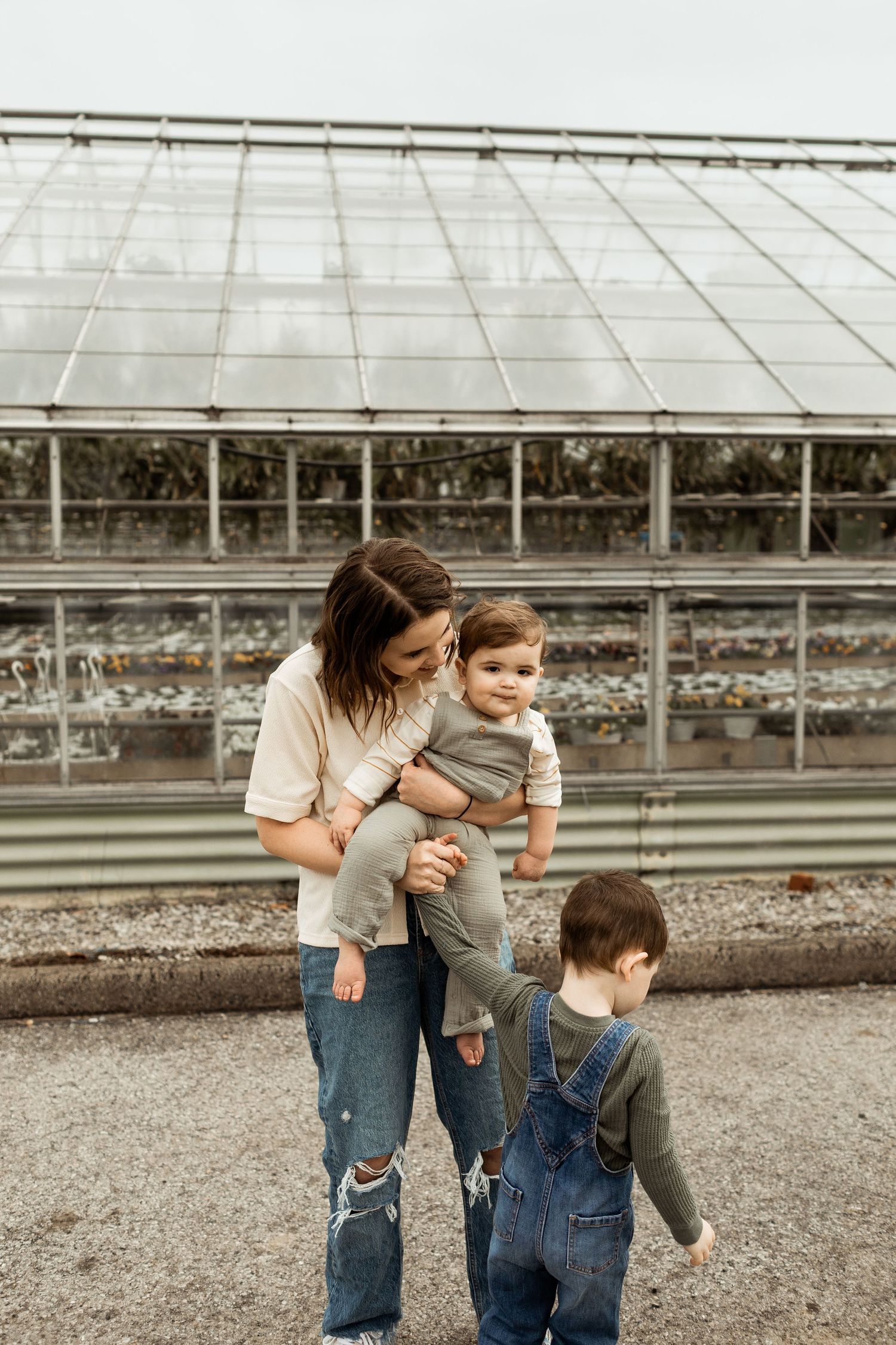 Mother and children standing outside a greenhouse on a cloudy day.