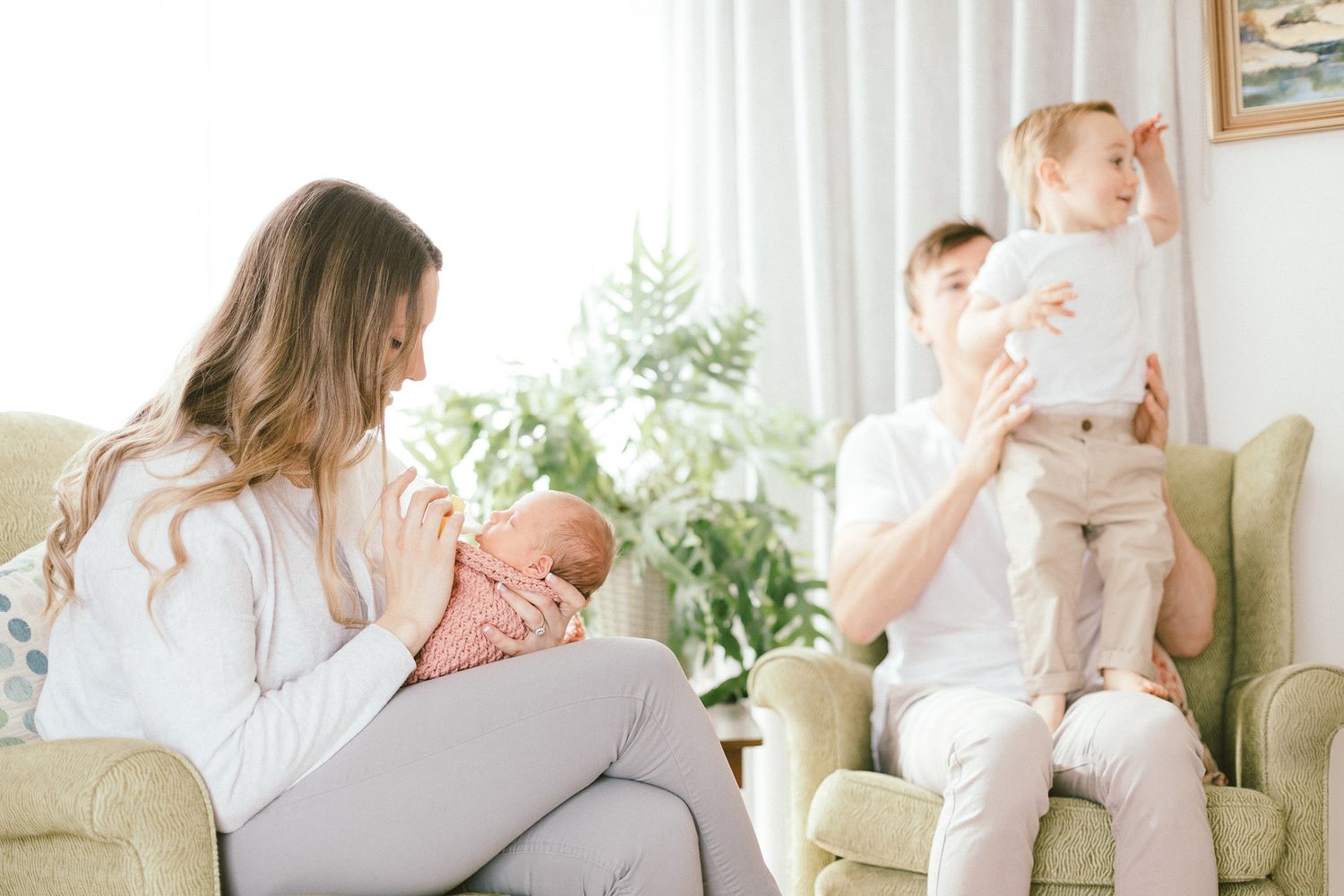 Bright living room scene with two children and caregiver during feeding time.