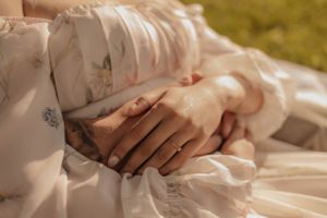 A close-up detail shot of hands resting on white fabric with delicate lace details.