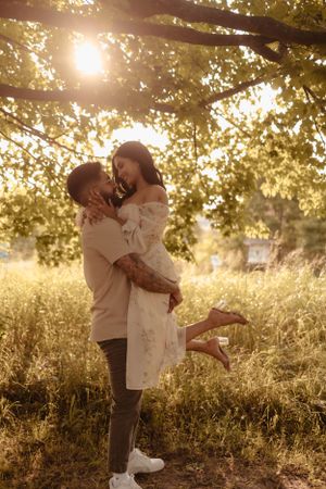 Romantic sunset embrace in a golden field with sunlight streaming through trees.
