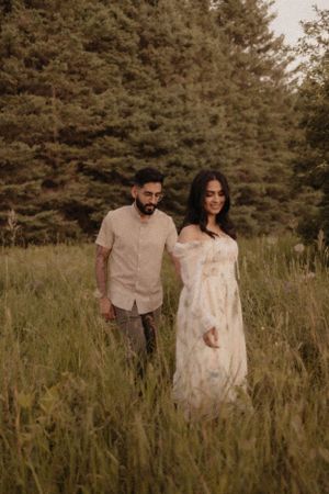 Couple walking through tall grass meadow with pine forest backdrop.