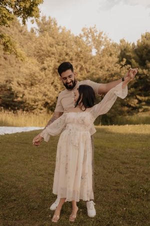 Dancing couple in white and beige outfits against golden sunset in grassy field.