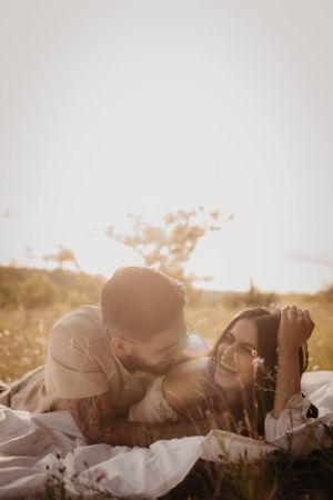 Couple laughing together on white blanket during outdoor sunset photoshoot.