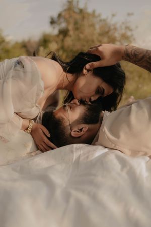 Intimate couple in white clothing sharing tender moment on blanket outdoors.