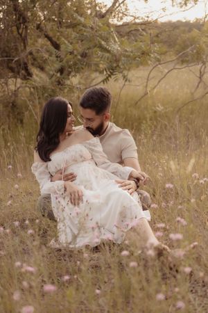 Romantic couple in white clothing embracing in wildflower meadow at sunset.